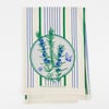A cream-colored flour-sack cloth with blue and green vertical stripes and a central circular rosemary illustration with small blue blossoms and a butterfly, printed with the text "VICTORYGARDENOFTOMORROW.COM" near the bottom.