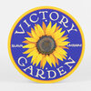 A round blue-and-yellow sign with a sunflower in the center and the words "VICTORY GARDEN" arched around it, with "SLAVA" on the left and "UKRAINI" on the right.