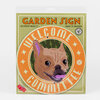 A round orange-and-green garden sign with the words "WELCOME COMMITTEE" and a illustrated French bulldog face in the center.