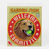 A packaged round garden sign with the words "WELCOME COMMITTEE" around a golden retriever illustration holding a green tennis ball, and the text "GARDEN SIGN" at the top.