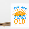 A folded white greeting card with a blue and orange sun graphic and the text "YOU ARE OLD" on the front, shown with a brown envelope.