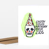 A folded greeting card with a hand-drawn skull wearing a party hat and the text "ENJOY YOUR BIRTHDAY WHILE YOU CAN" on the front.