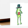 A folded greeting card with a green frog wearing a black top hat and holding a red heart on the front.