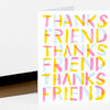 A folded greeting card with the words "THANKS FRIEND" repeated in large multicolored brush-style letters across the front.
