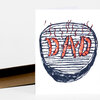A folded greeting card with a hand-drawn charcoal-style grill and red sausages spelling "DAD" on the front.