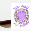 A folded greeting card or small card with the words "YOU HOG MY HEART" and a hedgehog illustration holding a large purple heart.