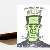 A folded greeting card with a stylized green Frankenstein-like face and the text "YOU MAKE ME FEEL ALIVE" on the front.