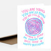A folded birthday card with a pink and blue spiral graphic and hand-lettered text that reads, "YOU ARE YOUNG YOU ARE SO YOUNG YOU ARE STILL SO YOUNG WHEN I SNAP MY FINGERS YOU WILL HAVE A HAPPY BIRTHDAY."