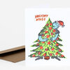 A folded holiday card with the text "HOLIDAY HUGS" above a colorful illustration of two blue characters hugging a decorated Christmas tree.