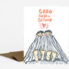 A folded greeting card printed with the words "GOOD TWO-GETHER" above an illustration of two people bundled under a striped blanket.