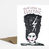 A folded greeting card with the text "OUR LOVE IS ELECTRIC" above a stylized illustrated face with a tall black hair silhouette and a lightning bolt through the hair.