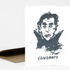 A folded greeting card or print with a black ink illustration of a vampire-like face and the word "CONGRATS" printed underneath.