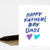 A folded greeting card with the cover text "HAPPY FATHER'S DAY DADS" in blue brush-style letters and two heart shapes in purple and turquoise.