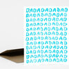 A folded greeting card with repeated turquoise "DAD" lettering across the front and a brown kraft paper envelope.