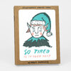 A kraft box set labeled "SIX LETTERPRESS PRINTED CARDS" and "W/ KRAFT ENVELOPES" featuring an illustrated elf face with the text "SO TIRED IS IT OVER YET?" on the front.