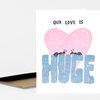 A folded greeting card with the text "OUR LOVE IS" above a large pink heart and the word "HUGE" in large blue letters with two small ants on top.