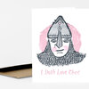 A folded greeting card with a stylized armored face illustration and the pink text "I Doth Love Thee" on the front.