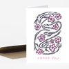A folded thank you card with a stylized black floral wreath design and pink flowers, with the words "THANK YOU" printed in pink on the front.