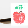 A folded greeting card with a large red painted apple and the words "THE BEST" in green on the front.