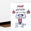 A folded greeting card with a hand-drawn illustration of a person lifting a barbell made of two birthday cakes and the text "PUMP IT UP THIS BIRTHDAY" on the front.