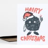 A folded holiday card shows a furry black cartoon character wearing a Santa hat and pointing upward, with the words "HAIRY" and "CHRISTMAS" in large coral letters.