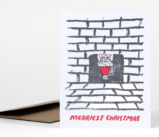 A white holiday greeting card with a sketchy black brick fireplace and a red-and-white Santa figure in the opening, with the text "MERRIEST CHRISTMAS" printed at the bottom.