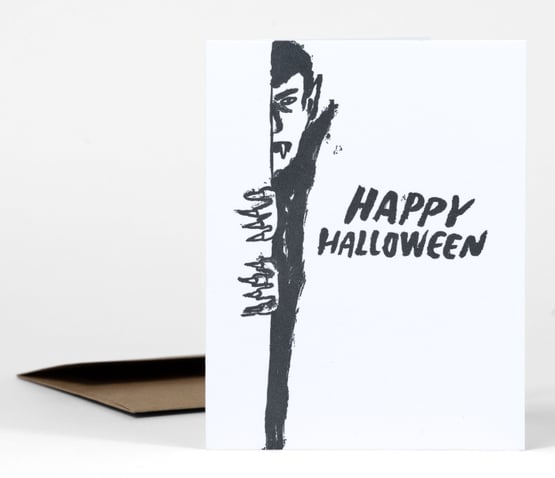 A black-and-white greeting card featuring a partial vampire illustration and the text "HAPPY HALLOWEEN" in bold brush lettering.